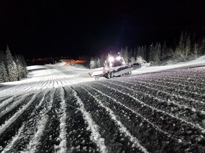 En pistmaskin bryter upp en backe.