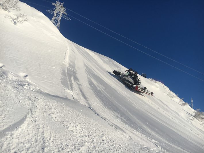 En pistmaskin arbetar under sol och blå himmel.