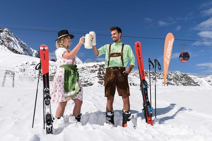 Kvinna iklädd Tyrolklänning skålar med man iklädd läderhosen.