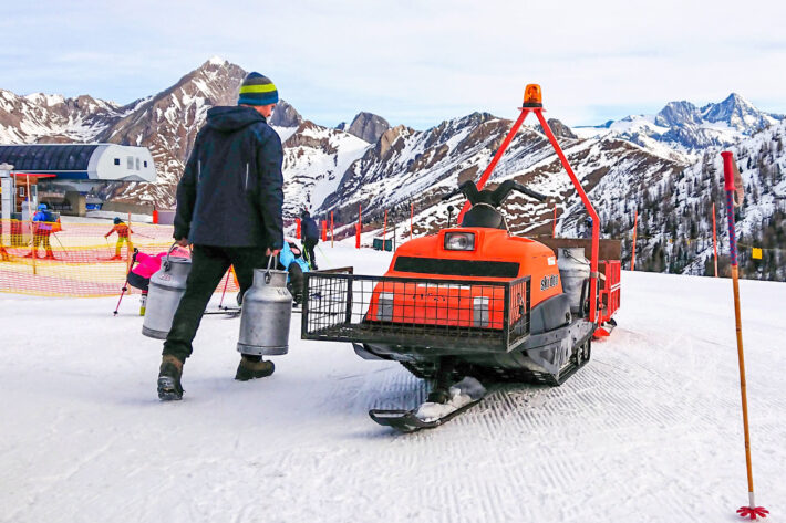 Mjölkbud lastar mjölkkannor på gammal orange snöskoter vid bergstationen av Goldried I, Grossglockner Resort Kals-Matrei.
