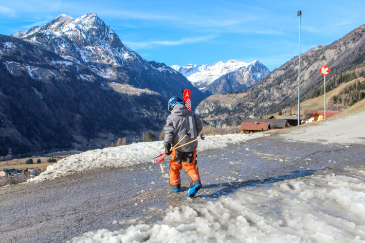Slaskig bilväg korsar pisten och Aron Rimfors bär skidorna över.