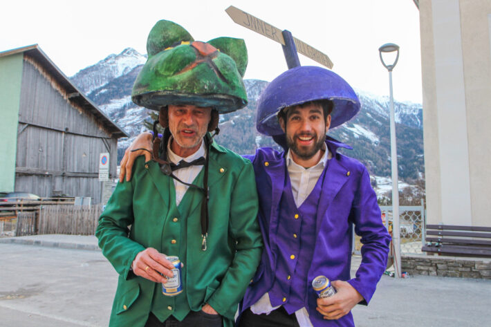 Faschingsumzug med två utklädda herrar: en till grön katt och en till lila vägvisare mot Innervillgraten.