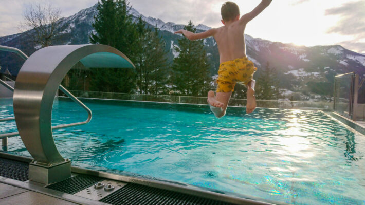 Aron Rimfors hoppar ner i utomhuspoolen på Hotel Goldried med halvvita berg i bakgrunden.